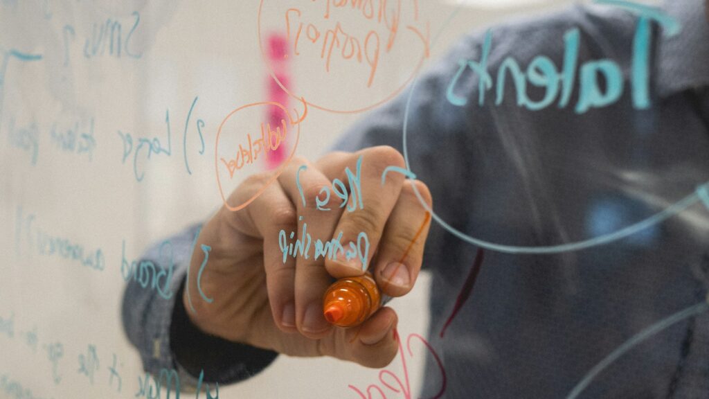 Person zeichnet Diagramme auf ein gläsernes Whiteboard