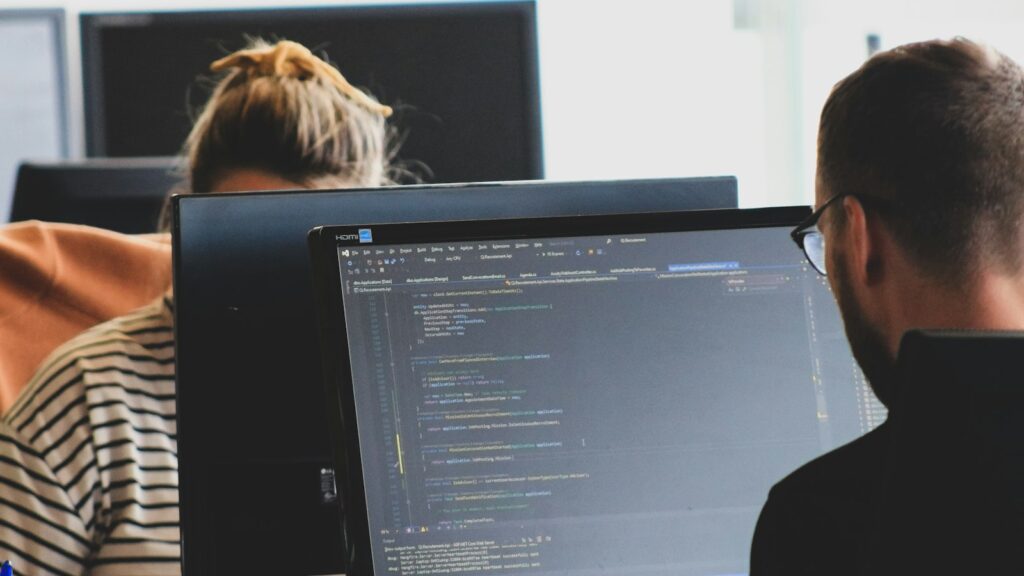 Zwei Gründer arbeiten an Monitoren mit Programmcode, um ein KI-Startup gründen zu können