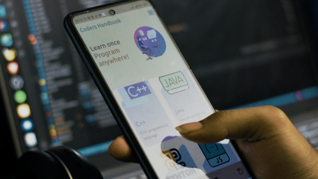 Person hält ein Smartphone vor einem Laptop und testet eine App
