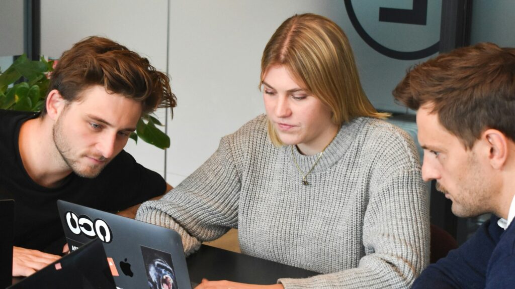 Drei Personen arbeiten gemeinsam an einem Laptop in einem Büro