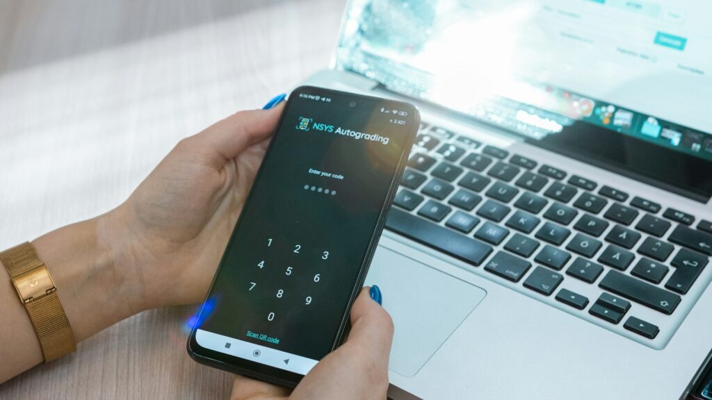 Person hält ein Smartphone vor einem aufgeklappten Laptop