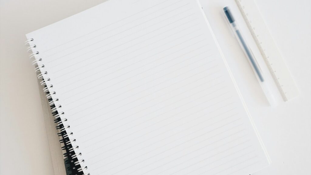 Leeres Spiralnotizbuch neben Tastatur und Stift