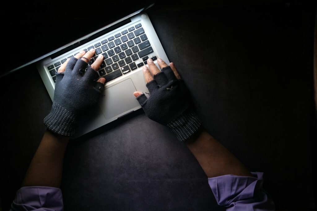 Person mit fingerlosen Handschuhen tippt im Dunkeln auf einem Laptop