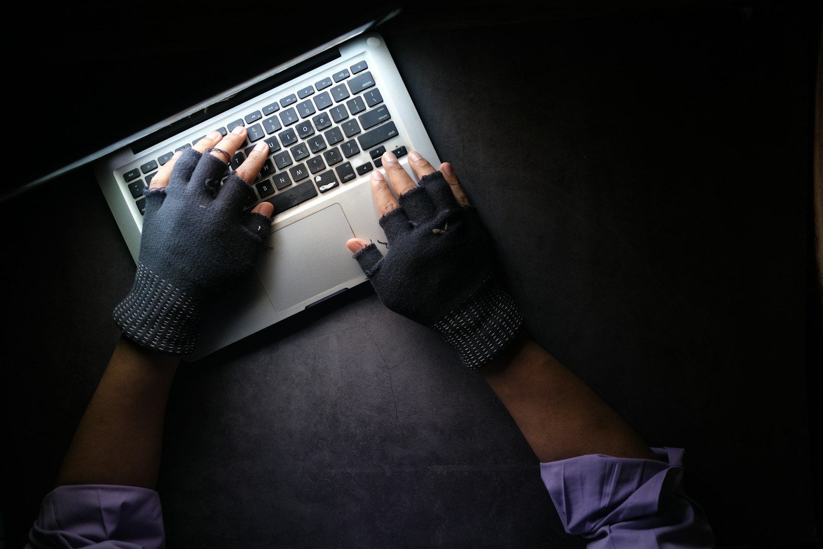 Person mit fingerlosen Handschuhen tippt im Dunkeln auf einem Laptop