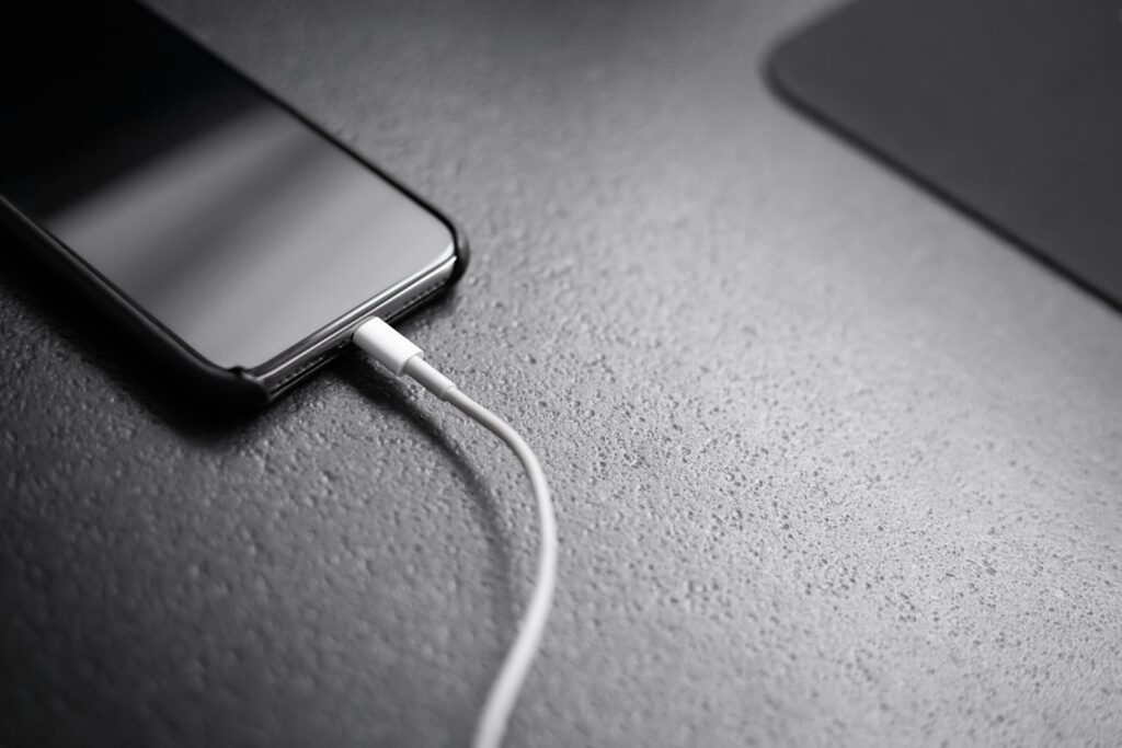 Schwarzes Smartphone mit angeschlossenem Ladekabel