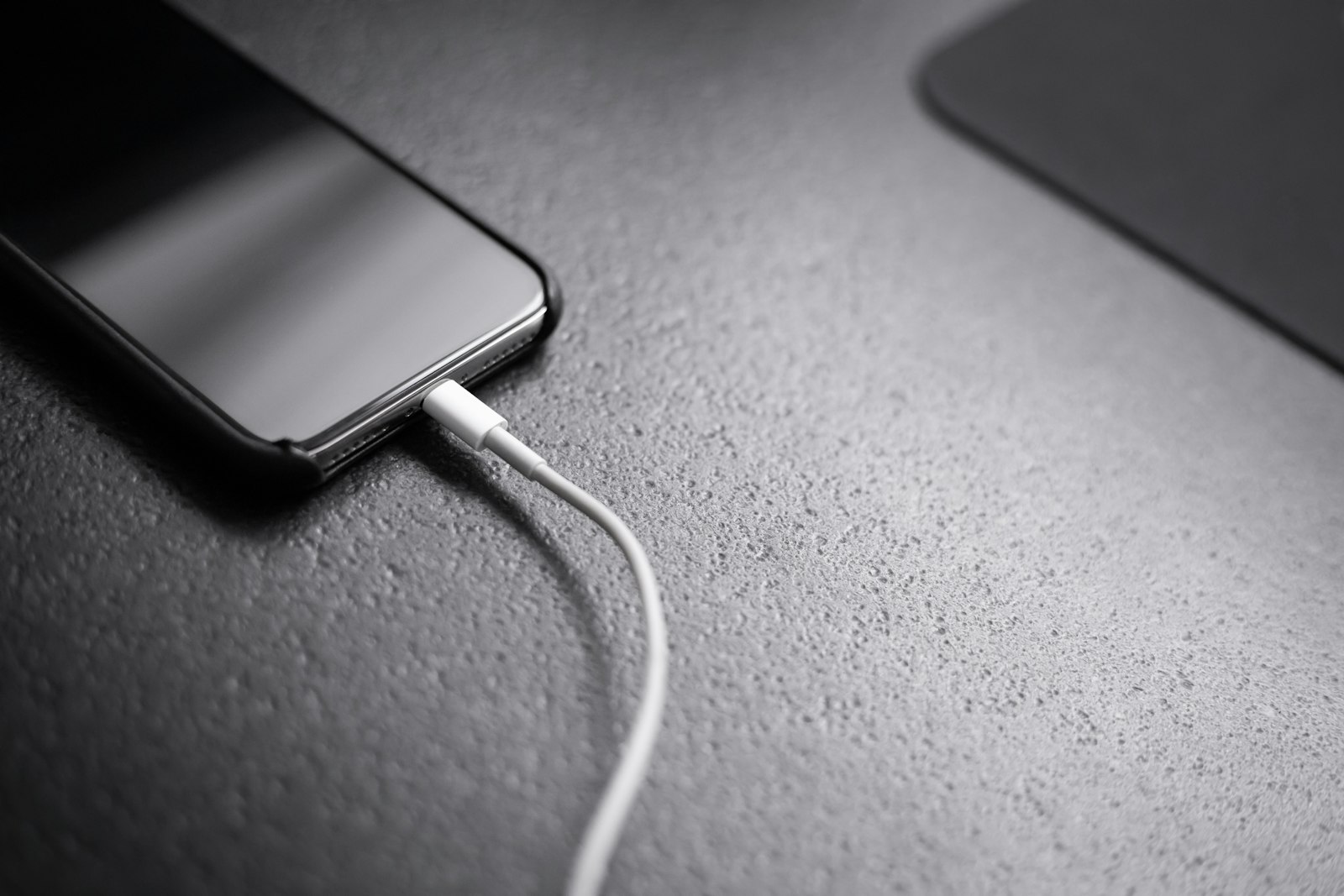 Schwarzes Smartphone mit angeschlossenem Ladekabel