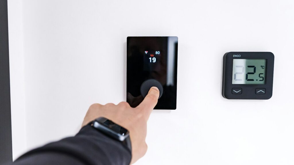 Finger stellt ein digitales Raumthermostat an der Wand ein